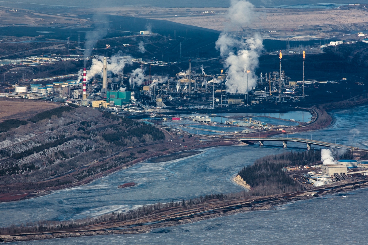 Smoke, steam, and gas flares rise from the Suncor upgrading facility. Reclamation efforts seen to the right, on what was once a tailing pond. Suncor has reclaimed only 7 per cent of their total land disturbance.